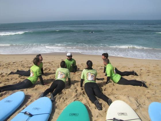 Un gruppo WeRoad in muta si riscalda su una spiaggia sabbiosa per una lezione di surf, con le tavole da surf in primo piano.
