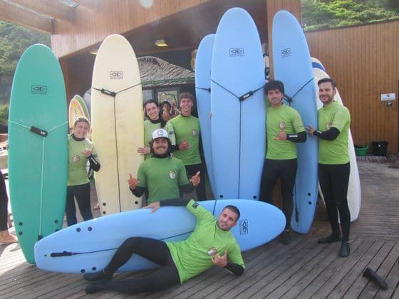 Un gruppo WeRoad in viaggio, con maglie verdi e mute abbinate, in posa con tavole da surf su un pontile di legno.