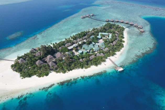 Vista aerea di un resort su un'isola tropicale con spiagge di sabbia bianca, palme e bungalow sull'acqua in un oceano turchese.