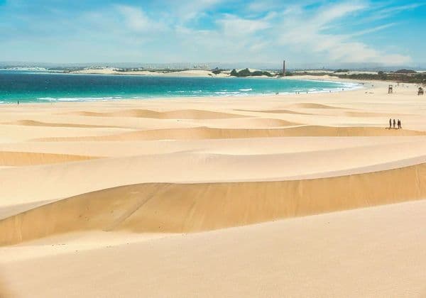 Un viaggio di gruppo WeRoad tra ampie dune di sabbia, affacciate su un oceano turchese sotto un cielo parzialmente nuvoloso.