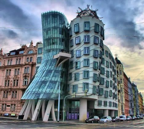 Un moderno edificio deconstructivista, con una torre de cristal retorcida y una torre de hormigón, se erige en una esquina bajo un cielo nublado.