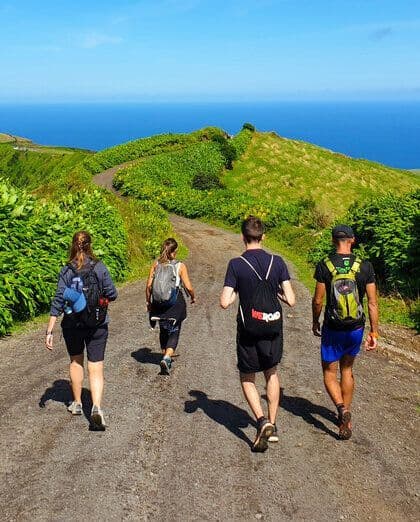 Eine WeRoad Gruppenreise wandert einen unbefestigten Weg auf einem grünen Küstenhügel hinunter, mit Blick auf das Meer.