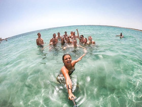 Une femme prend un selfie de son groupe WeRoad nageant dans une mer turquoise et claire par une journée ensoleillée.