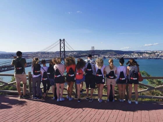 Un gruppo WeRoad, visto di spalle, ammira da un punto panoramico un grande ponte sospeso sull'acqua.