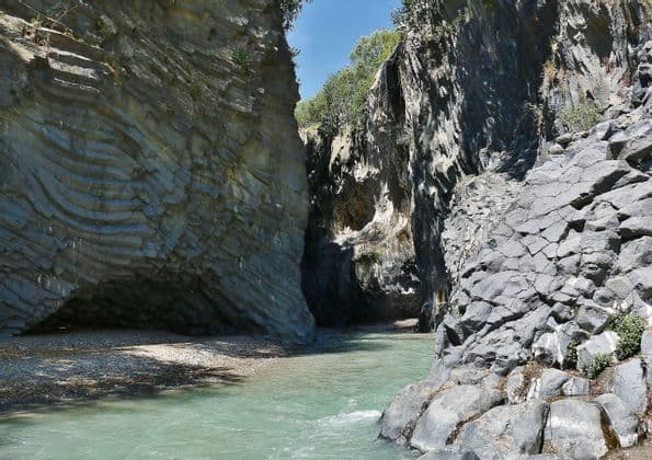 Un fiume con acqua turchese si snoda attraverso una gola stretta con alte pareti di roccia vulcanica stratificata e fratturata.