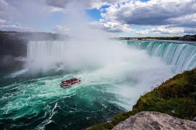 Una barca turistica con un gruppo WeRoad naviga tra le acque nebbiose e turchesi ai piedi di una potente cascata.