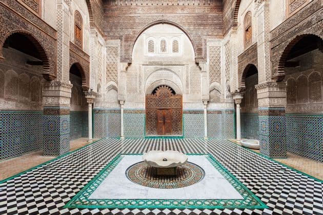 Un ornamentado patio interior con un suelo de damero blanco y negro, paredes de mosaico y una fuente central.