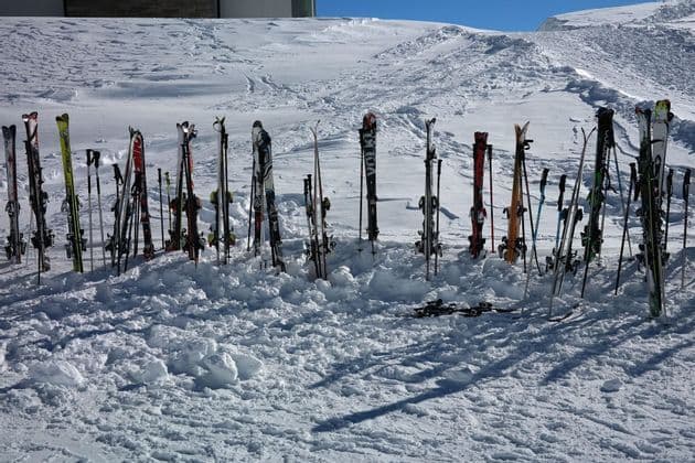 Esquís y bastones clavados verticalmente en la nieve profunda de una ladera soleada de montaña.