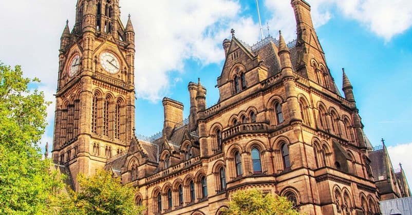 Una vista dal basso di un elaborato edificio in pietra in stile gotico con una grande torre dell'orologio, contro un cielo azzurro con nuvole.