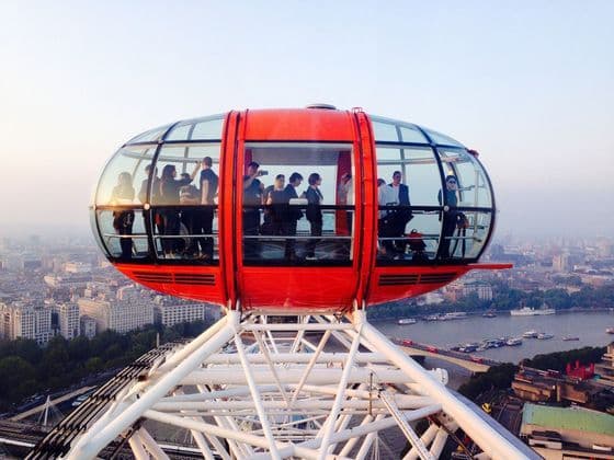 Un viaje en grupo de WeRoad dentro de una cápsula roja de una gran noria, con vistas a un paisaje urbano y un río al atardecer.