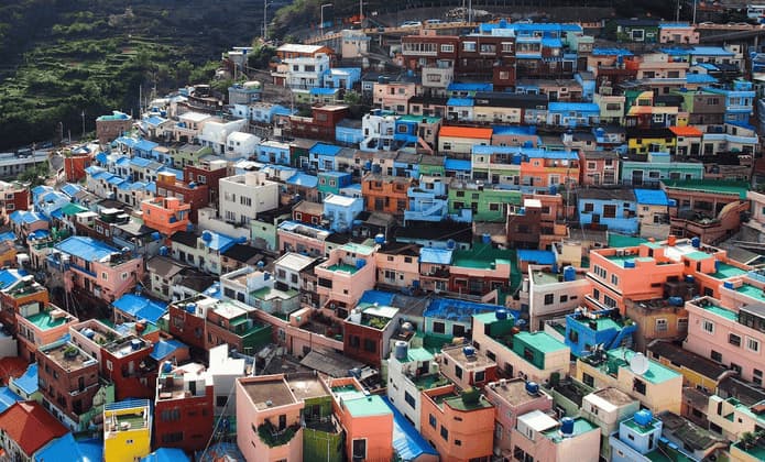 Case colorate con tetti blu brillanti sono addossate strettamente su un ripido versante verde in un villaggio denso.