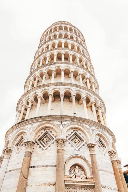 A low-angle view looking up at the ornate, circular tiers of a white marble tower with many arches and columns against a bright sky.
