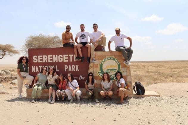 Un gruppo WeRoad in posa per una foto sul e di fronte al grande cartello d'ingresso del Parco Nazionale del Serengeti.