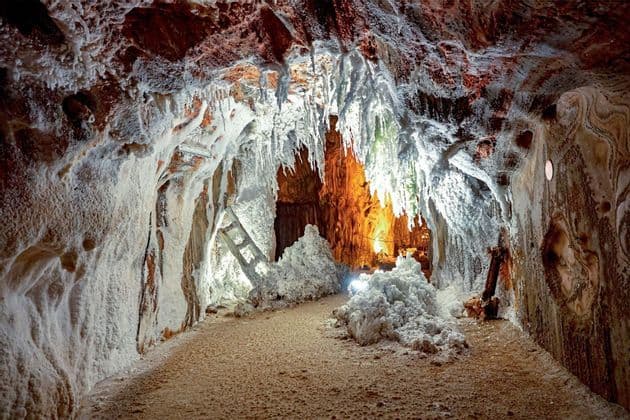 Das beleuchtete Innere einer Salzhöhle, mit weißen kristallinen Formationen und Stalaktiten an Wänden und Decke.