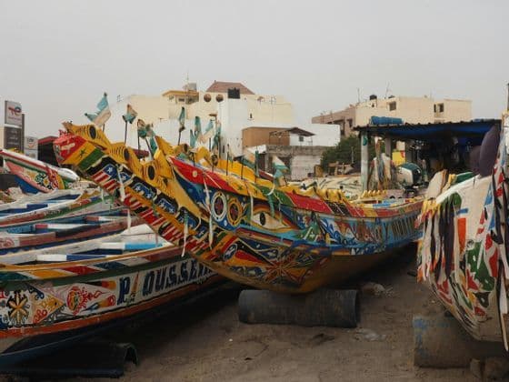 Barcos tradicionales bellamente pintados con patrones coloridos, banderas y un ojo grande, descansando en una playa de arena.