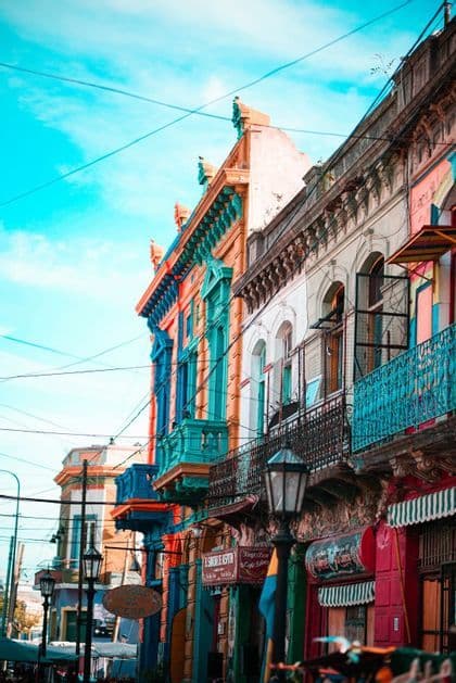 Vista en contrapicado de edificios de colores vivos con balcones ornamentados, bajo un cielo azul intenso con cables eléctricos que se cruzan.
