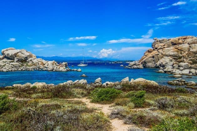 Ein weißes Segelboot ankert in einer ruhigen, türkisfarbenen Bucht, eingerahmt von großen, glatten Felsformationen unter strahlend blauem Himmel.