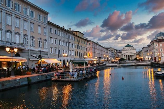 Un canale cittadino al tramonto, con persone che cenano nei ristoranti sul lungomare e luci che si riflettono sull'acqua.