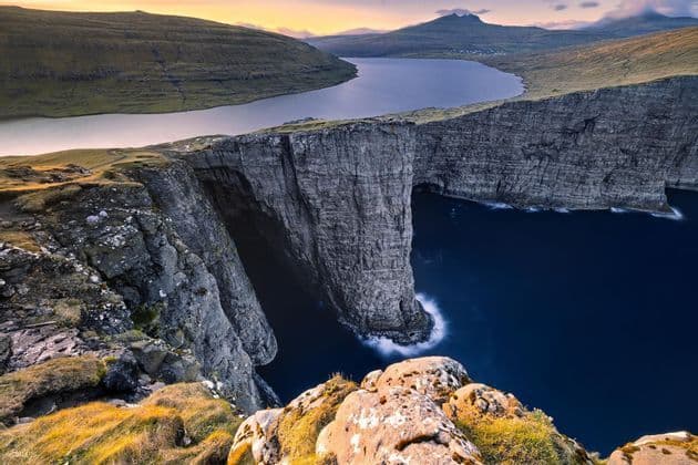 Un grande lago si trova sul bordo di un'alta scogliera, affacciato sul profondo oceano blu, con verdi colline ondulate in lontananza.