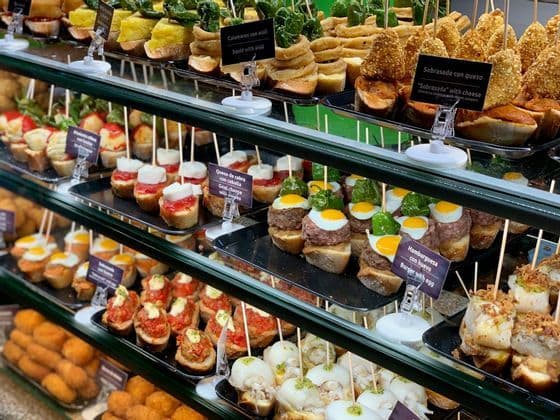A variety of Spanish tapas, known as pintxos, neatly arranged on multiple shelves inside a glass display case.