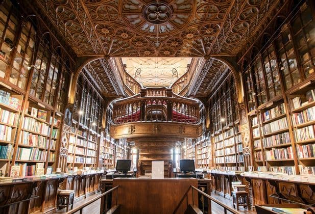 L'interno di una sfarzosa biblioteca in legno a più piani con una grande scalinata centrale e scaffali a tutta altezza.