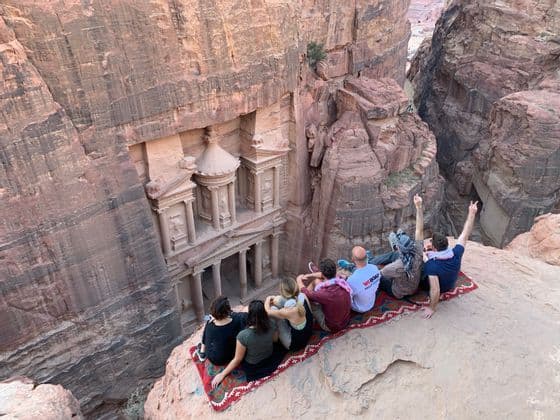 Un grupo de WeRoad se sienta en la arena roja del desierto alrededor de una tetera, con montañas al fondo durante el atardecer.