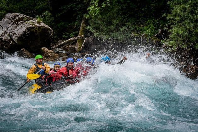 Un viaggio di gruppo WeRoad, indossando caschi e giubbotti di salvataggio, fa rafting in acque bianche turbolente, pagaiando tra grandi spruzzi.