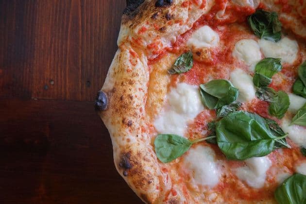Un primo piano di una pizza Margherita napoletana con mozzarella e basilico fresco su un tavolo di legno scuro.