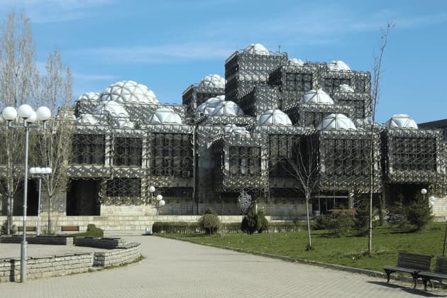 Un edificio architettonico brutalista con diverse sezioni cubiche ricoperto da un reticolo metallico e sormontato da cupole bianche.