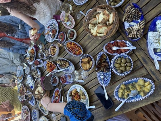 Vista dall'alto di un gruppo WeRoad in viaggio che condivide antipasti serviti in tanti piccoli piatti su un tavolo di legno.
