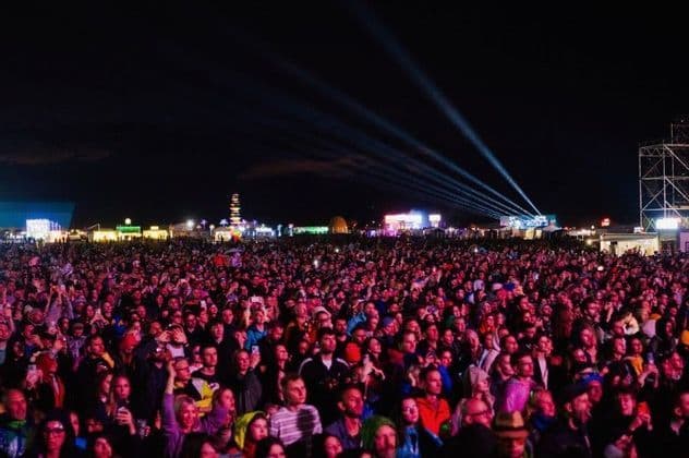 Una grande folla di persone a un festival di musica all'aperto di notte, con i riflettori che illuminano il cielo scuro.