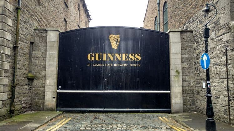 Das schwarze Eingangstor zur Guinness St. James's Gate Brauerei in Dublin, eingebettet zwischen zwei Steingebäuden an einer Kopfsteinpflasterstraße.