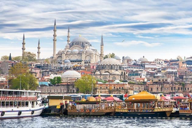 Una grande moschea con cupole e minareti si affaccia su un lungomare cittadino dove diverse imbarcazioni sono ormeggiate sull'acqua.