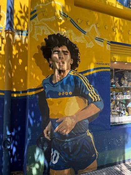 Un murale colorato di Diego Maradona, calciatore, dipinto su una parete di un edificio in blu e giallo.