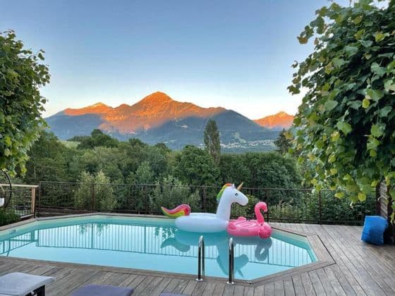 Une licorne et un flamant rose gonflables flottent dans une piscine avec vue sur des montagnes boisées éclairées par le coucher du soleil.