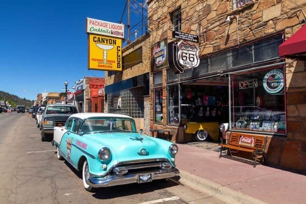 A vintage light-blue car parked on a street in front of storefronts with Route 66 signs.