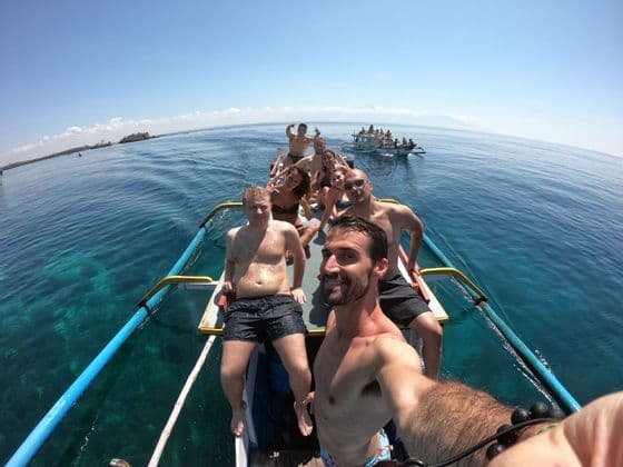 Un grupo de WeRoad se toma una selfie en una barca estrecha mientras navega sobre aguas turquesas cristalinas en un día soleado.