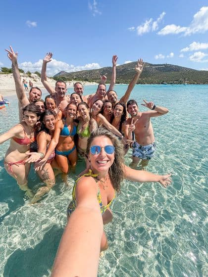 Un gruppo WeRoad sorride e posa per un selfie in un'acqua cristallina e turchese, accanto a una spiaggia sabbiosa.