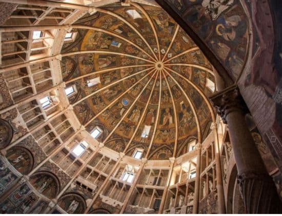 Una vista verso l'alto di una grande cupola dipinta all'interno di un edificio storico, caratterizzata da affreschi religiosi, gallerie concentriche e finestre ad arco.