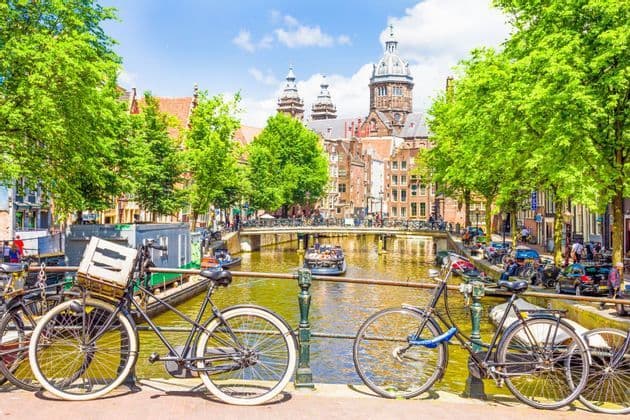 Two bicycles parked on a bridge overlooking a canal with historic buildings and green trees under a blue sky.