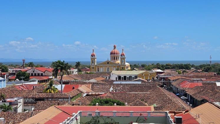 Ein Blick von oben auf eine Stadt mit Terrakotta-Dächern, einer zentralen gelben Kathedrale mit roten Kuppeln und dem Meer im Hintergrund.