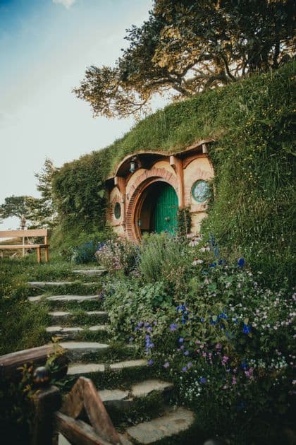 A hobbit-style home with a round green door built into a grassy hill, with stone steps leading up through a garden of flowers.