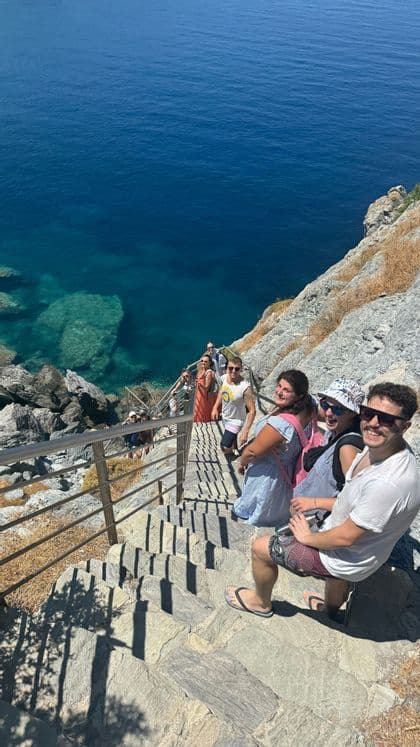 Un gruppo WeRoad sorride salendo una scalinata in pietra costruita nella scogliera che si affaccia sul mare blu.
