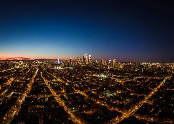 An aerial view of a sprawling city at dusk, with illuminated streets leading to a glowing skyline of skyscrapers.