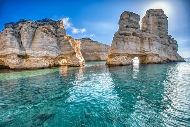 Formazioni rocciose bianche con archi naturali si ergono in acque turchesi e limpide sotto un cielo azzurro e soleggiato.