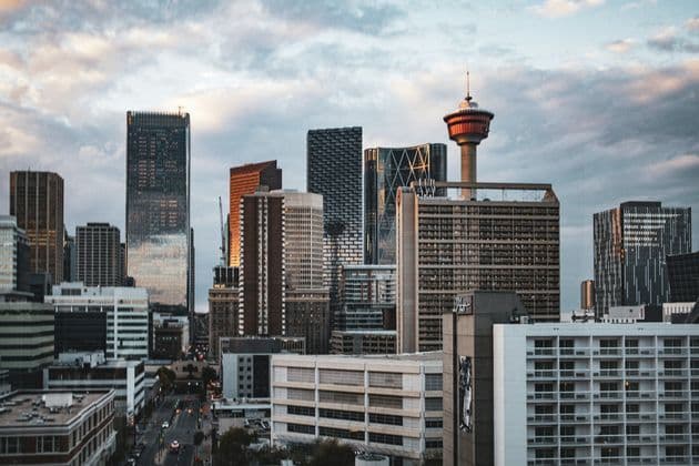 A dense cityscape with modern skyscrapers and a prominent observation tower under a cloudy sky at dusk.