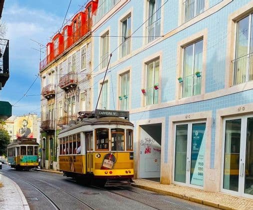 Un tram giallo d'epoca percorre i binari lungo una strada curva, costeggiando edifici con facciate di piastrelle colorate.