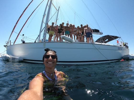 Eine lächelnde Frau macht ein Selfie aus dem Wasser, während eine WeRoad-Gruppenreise an Deck eines Segelbootes posiert.
