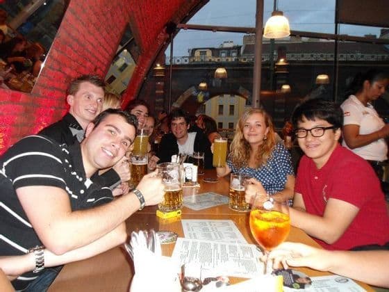 Des membres d'un groupe WeRoad en voyage sourient pour une photo, attablés avec des bières et des cocktails dans un bar.