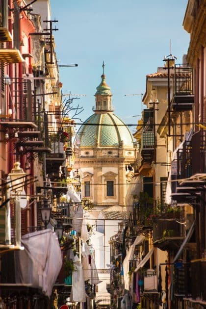 A green-tiled dome of a church is visible at the end of a narrow street lined with colourful buildings and hanging laundry.